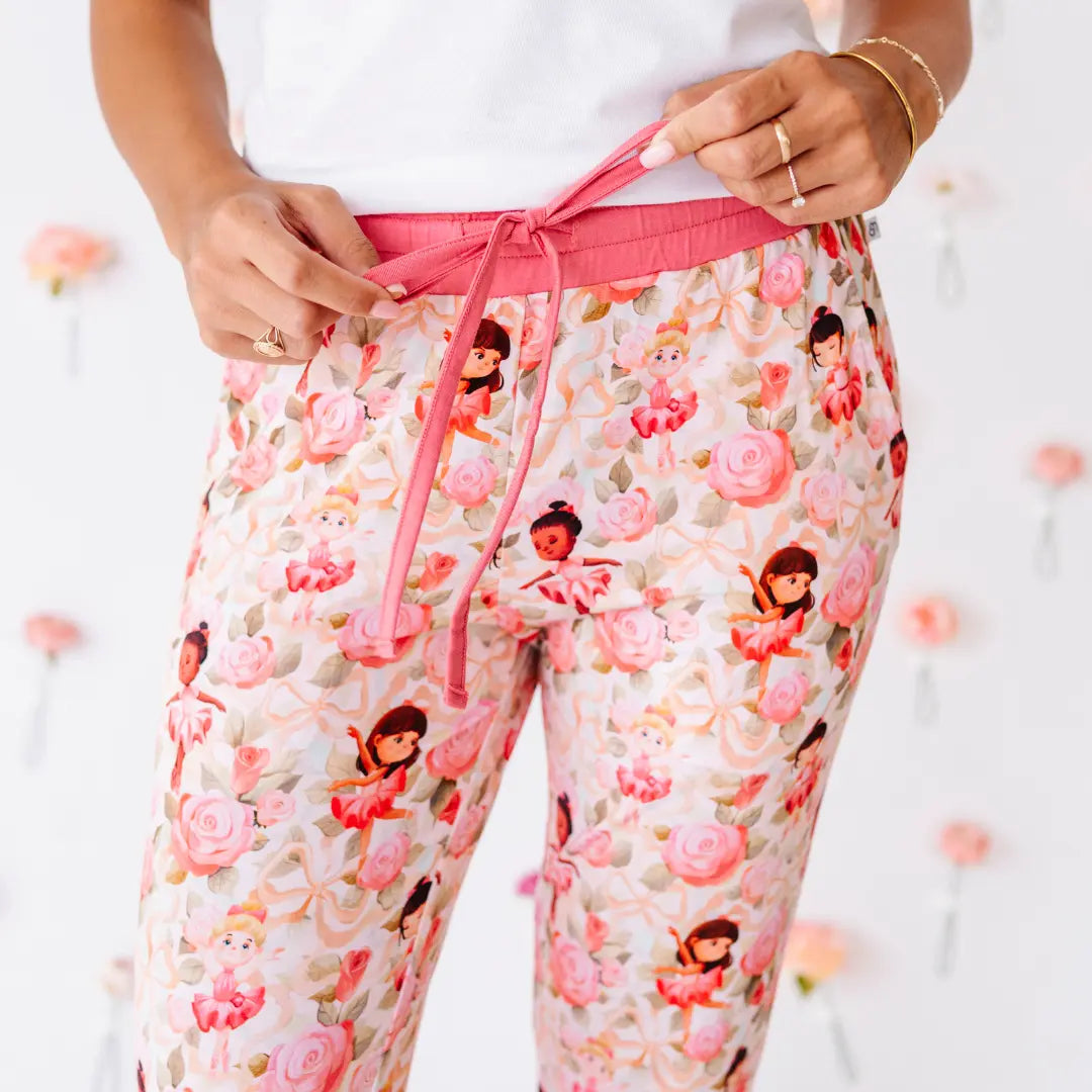 Close-up of a woman tying the rose-pink drawstring of pajama pants printed with pink roses and little ballerinas.
